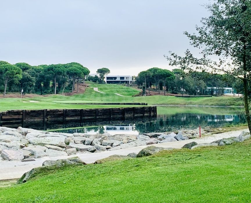 Läckert hål med vatten och green på PGA Catalunya och klubbhuset långt bort i bakgrunden.
